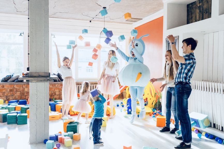 Children and adults playing fun indoor party games with colourful foam blocks beside a bouncy castle, provided by Bizi Bouncers UK for 10 Fun Indoor Party Games to Play Around a Bouncy Castle.