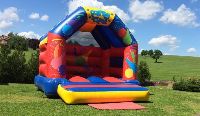 Colorful inflatable bouncy castle with a roof, decorated with balloons and party designs, set up on a grassy field under a blue sky