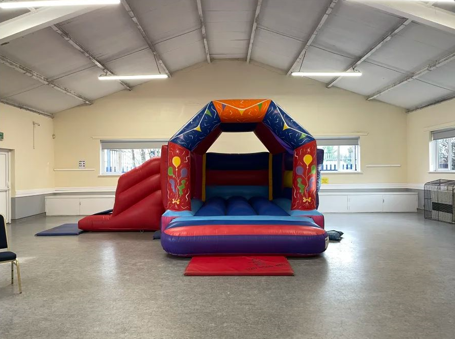 Indoor bouncy castle with slide provided by Bizi Bouncers UK for Bouncy Castle Hire Stratford, set up safely inside a bright community hall.