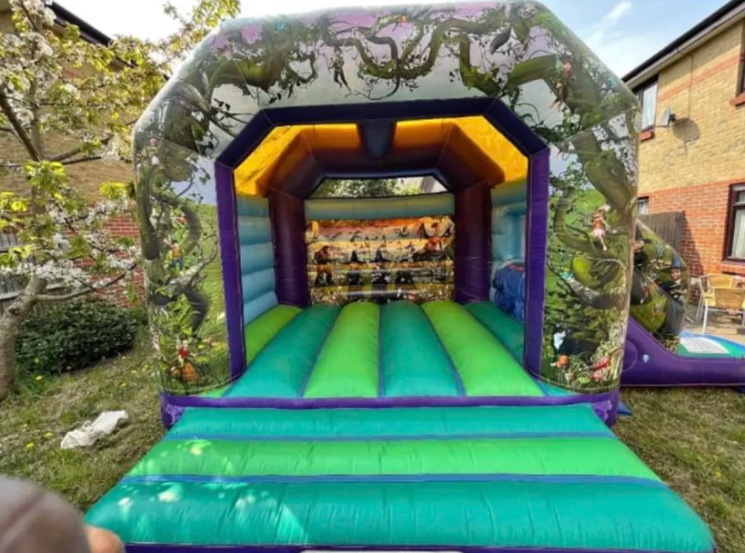 Enchanted forest-themed bouncy castle with vibrant green and purple design, featuring fairy artwork, set up outdoors by Bizi Bouncers UK
